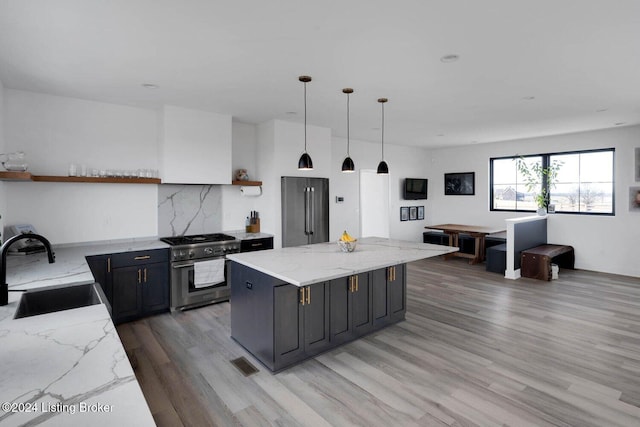 kitchen with sink, stainless steel range, decorative light fixtures, light hardwood / wood-style floors, and light stone counters