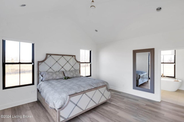 bedroom with high vaulted ceiling, light wood-type flooring, connected bathroom, and multiple windows