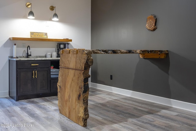 bar featuring light wood-type flooring, hanging light fixtures, and sink