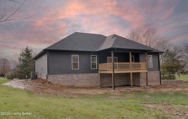 back house at dusk featuring a wooden deck, a yard, and cooling unit