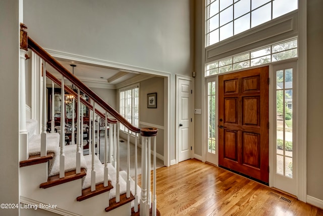 entryway with a high ceiling, light hardwood / wood-style floors, crown molding, and a healthy amount of sunlight