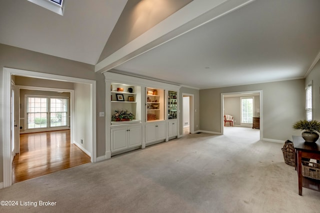 unfurnished living room featuring built in features, light colored carpet, lofted ceiling, and ornamental molding