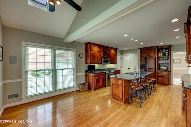 kitchen with stainless steel appliances, light hardwood / wood-style flooring, lofted ceiling, a kitchen bar, and a center island with sink