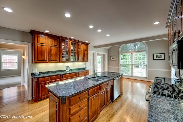 kitchen with sink, stainless steel appliances, an island with sink, dark stone counters, and light wood-type flooring