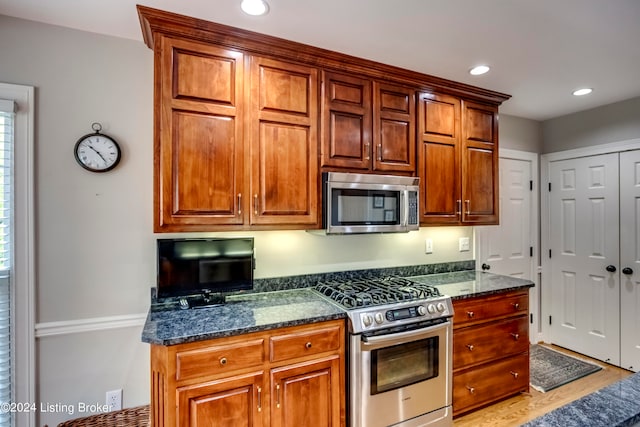 kitchen with light hardwood / wood-style floors, appliances with stainless steel finishes, and dark stone counters