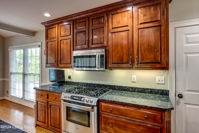 kitchen with light hardwood / wood-style flooring, beamed ceiling, dark stone counters, and appliances with stainless steel finishes