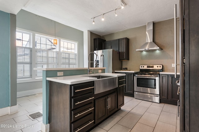 kitchen with dark brown cabinetry, sink, wall chimney exhaust hood, stainless steel appliances, and a kitchen island with sink