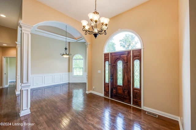 entrance foyer with decorative columns, an inviting chandelier, a wealth of natural light, and dark wood-type flooring