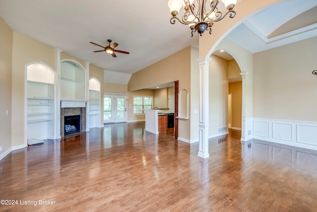 unfurnished living room featuring ornate columns, a premium fireplace, built in features, hardwood / wood-style floors, and ceiling fan with notable chandelier