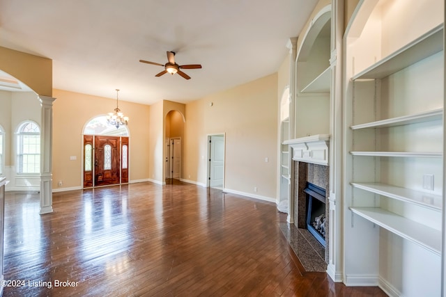 unfurnished living room with ornate columns, a high end fireplace, dark wood-type flooring, and ceiling fan with notable chandelier