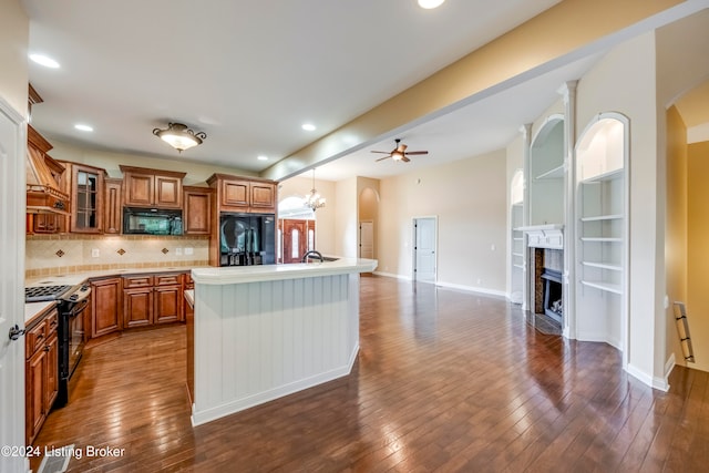 kitchen featuring ceiling fan with notable chandelier, black appliances, a fireplace, dark hardwood / wood-style floors, and a kitchen island