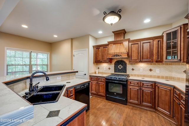 kitchen featuring backsplash, black appliances, sink, light hardwood / wood-style floors, and custom range hood