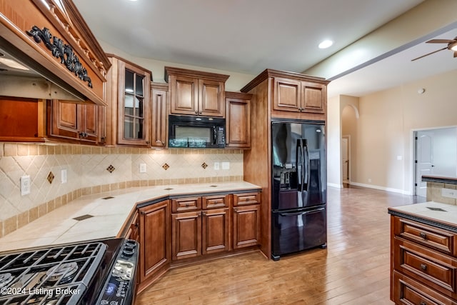 kitchen with light wood-type flooring, backsplash, custom exhaust hood, ceiling fan, and black appliances