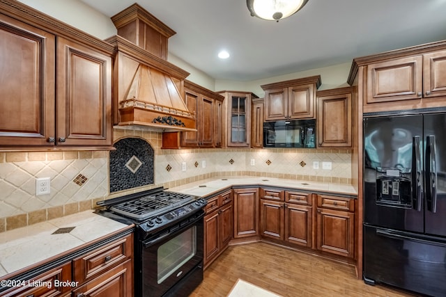 kitchen with black appliances, light hardwood / wood-style floors, premium range hood, and tasteful backsplash