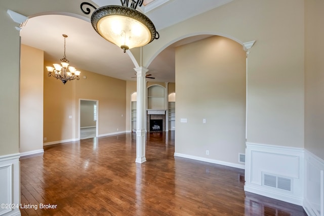 unfurnished room with a notable chandelier, dark hardwood / wood-style flooring, and ornate columns