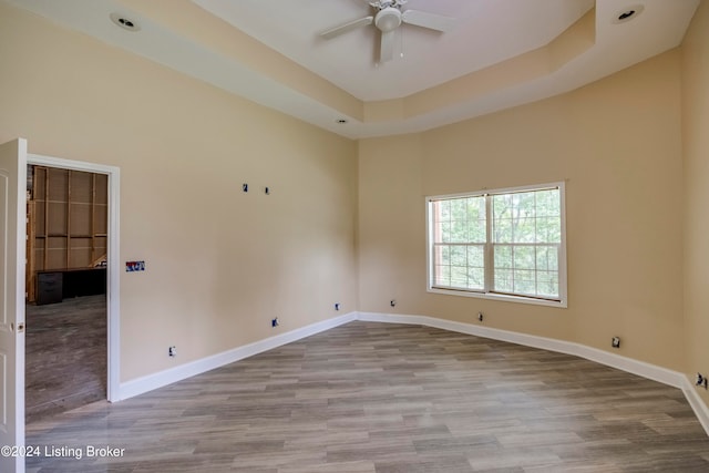 empty room featuring a raised ceiling, ceiling fan, a high ceiling, and light wood-type flooring