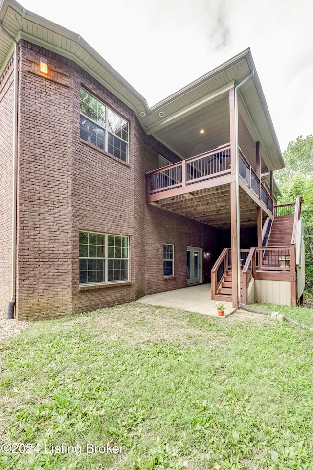 rear view of property featuring a lawn, a wooden deck, and a patio