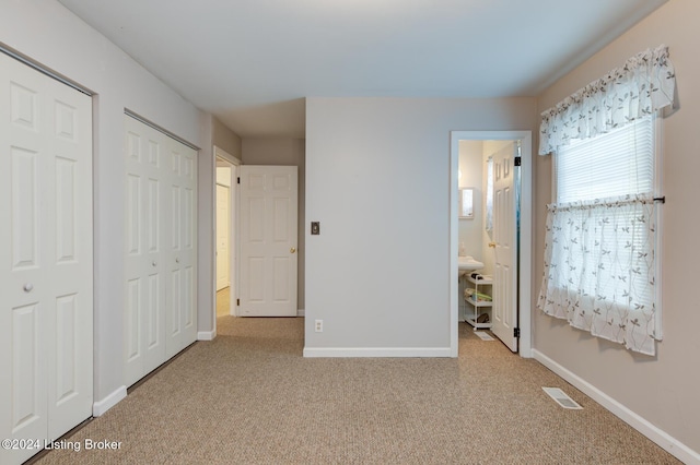 unfurnished bedroom with ensuite bathroom, light colored carpet, and two closets