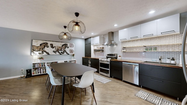 kitchen with pendant lighting, stainless steel appliances, white cabinetry, and wall chimney range hood