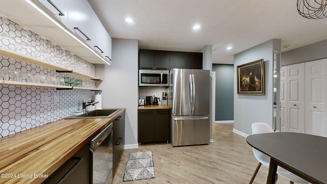 kitchen with backsplash, sink, appliances with stainless steel finishes, butcher block countertops, and light hardwood / wood-style floors