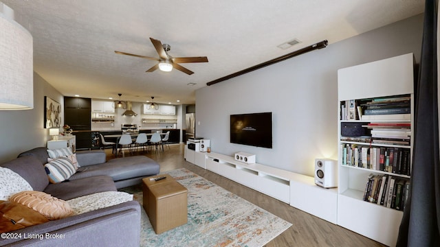 living room with hardwood / wood-style floors, ceiling fan, ornamental molding, and a textured ceiling