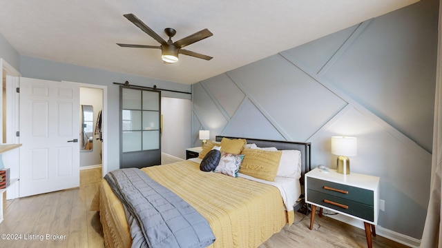 bedroom with ceiling fan, a barn door, and light wood-type flooring