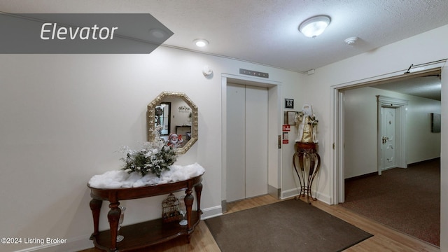 hall with a textured ceiling, elevator, and hardwood / wood-style flooring