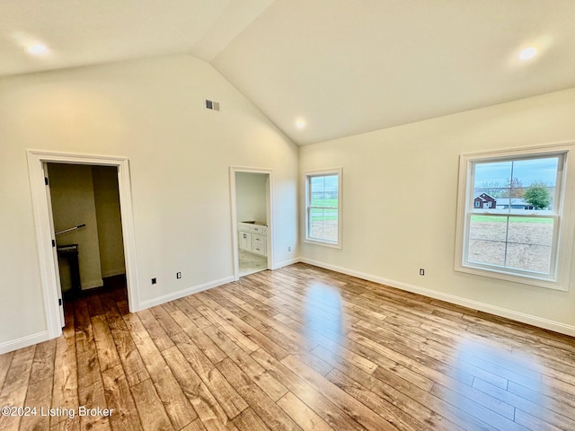 unfurnished bedroom with light wood-type flooring, a walk in closet, high vaulted ceiling, and ensuite bath