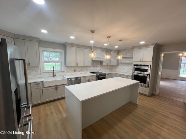 kitchen featuring appliances with stainless steel finishes, sink, light hardwood / wood-style floors, a kitchen island, and hanging light fixtures