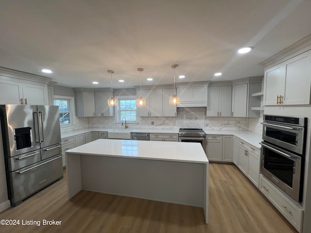 kitchen with sink, light wood-type flooring, decorative light fixtures, a kitchen island, and stainless steel appliances