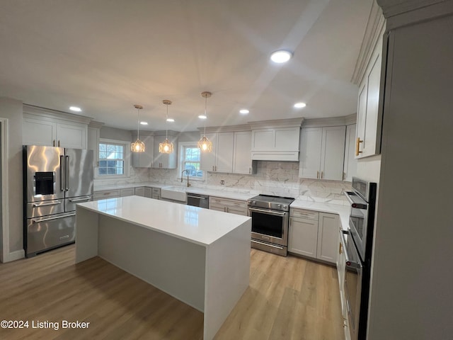 kitchen featuring hanging light fixtures, appliances with stainless steel finishes, decorative backsplash, a kitchen island, and light wood-type flooring