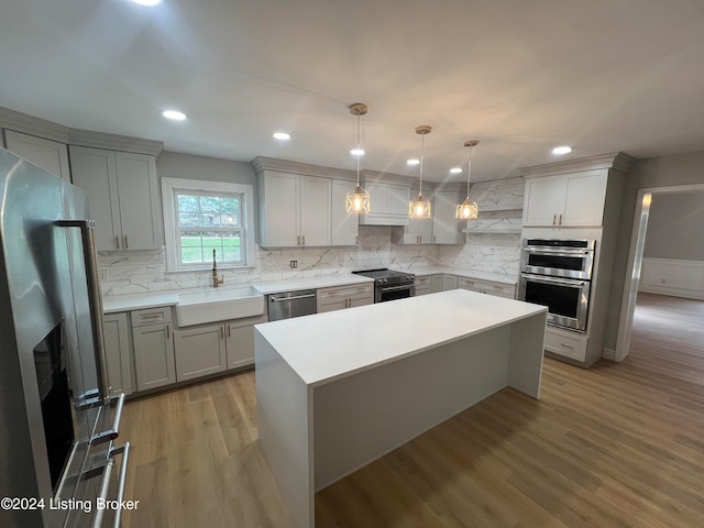 kitchen featuring sink, light wood-type flooring, appliances with stainless steel finishes, decorative light fixtures, and a kitchen island