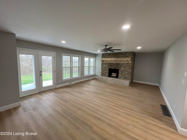 unfurnished living room featuring a stone fireplace, ceiling fan, french doors, and light hardwood / wood-style floors