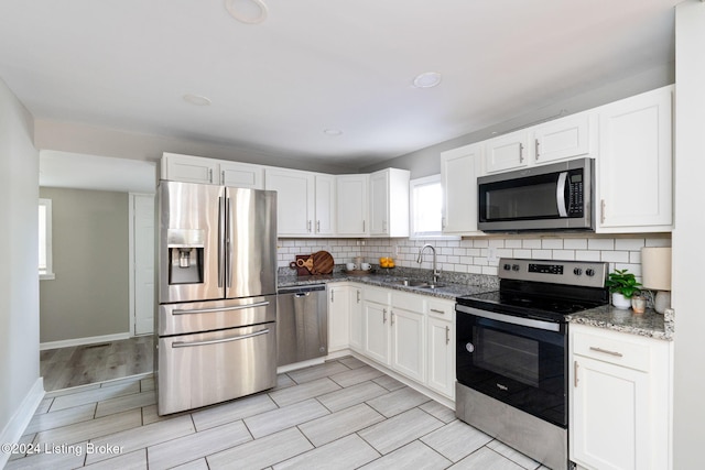 kitchen featuring white cabinetry, sink, stainless steel appliances, light stone counters, and light wood-type flooring