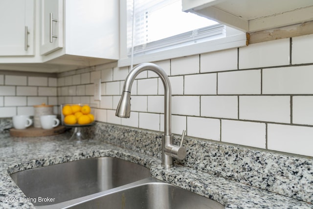 room details featuring decorative backsplash, sink, white cabinets, and light stone counters