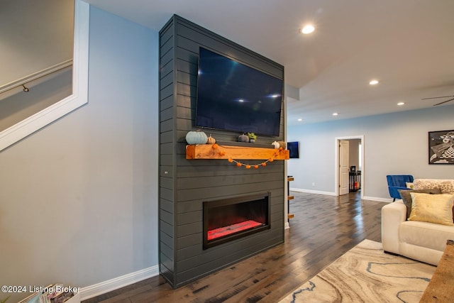 living room featuring dark hardwood / wood-style floors, a large fireplace, and ceiling fan