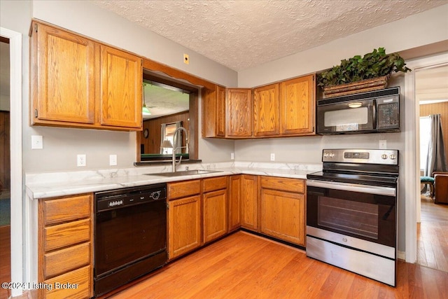 kitchen featuring a textured ceiling, sink, light hardwood / wood-style flooring, and black appliances