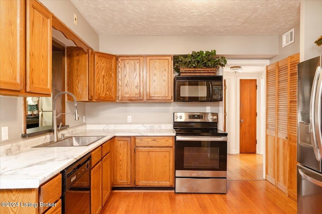 kitchen featuring black appliances, a textured ceiling, sink, and light hardwood / wood-style flooring