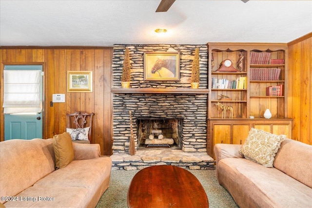 carpeted living room with ceiling fan, a stone fireplace, wood walls, crown molding, and a textured ceiling