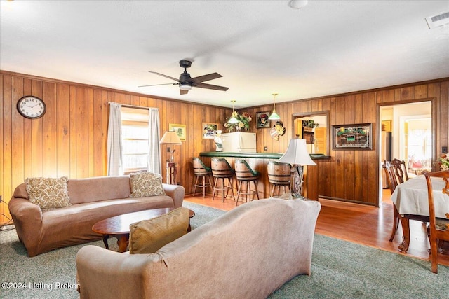 living room with wooden walls, indoor bar, hardwood / wood-style flooring, ceiling fan, and ornamental molding