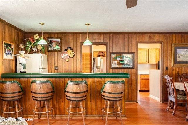 bar featuring hardwood / wood-style floors, stainless steel fridge, white fridge, and decorative light fixtures