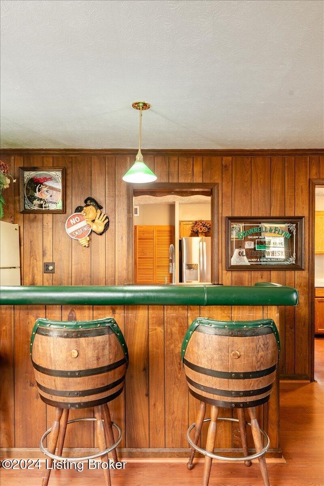 bar featuring hanging light fixtures, stainless steel refrigerator with ice dispenser, white refrigerator, wood walls, and hardwood / wood-style flooring