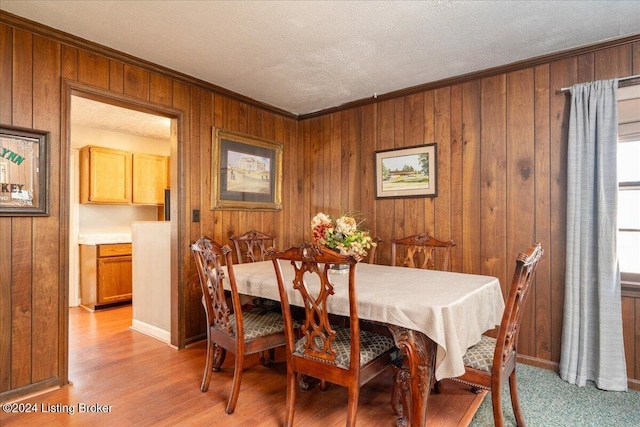 dining area featuring a textured ceiling, light wood-type flooring, crown molding, and wooden walls