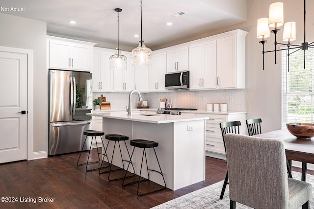 kitchen with white cabinetry, dark hardwood / wood-style flooring, pendant lighting, a center island with sink, and appliances with stainless steel finishes