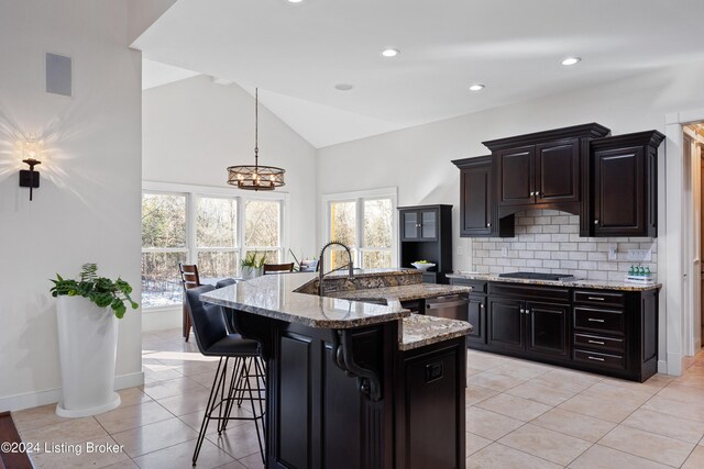 kitchen with pendant lighting, light stone countertops, light tile patterned floors, and a kitchen island with sink