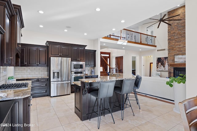 kitchen featuring a kitchen island with sink, light tile patterned floors, light stone countertops, a kitchen bar, and stainless steel appliances