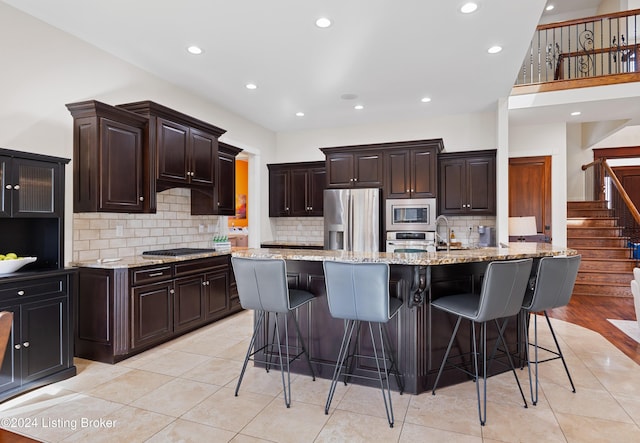 kitchen featuring a breakfast bar, a center island with sink, appliances with stainless steel finishes, light hardwood / wood-style floors, and light stone counters