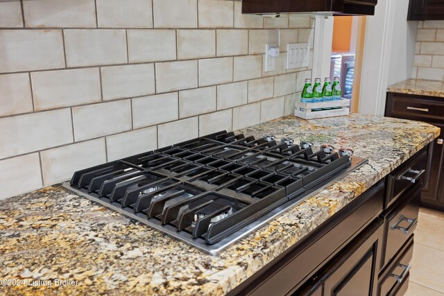 details featuring dark brown cabinets, gas stovetop, light stone counters, and tasteful backsplash