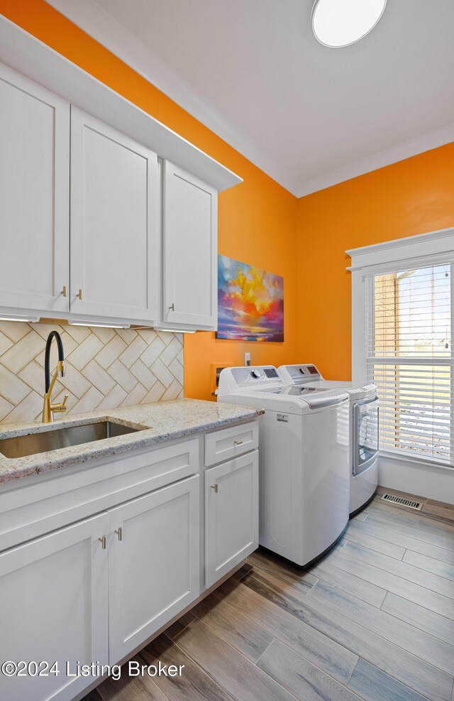 clothes washing area featuring cabinets, light wood-type flooring, washing machine and dryer, and sink