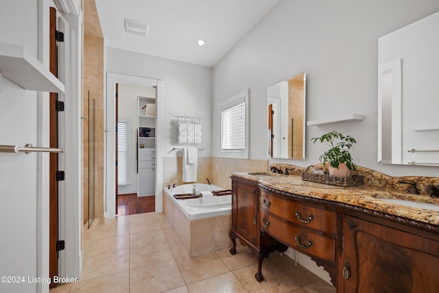 bathroom featuring tile patterned flooring, vanity, and a relaxing tiled tub